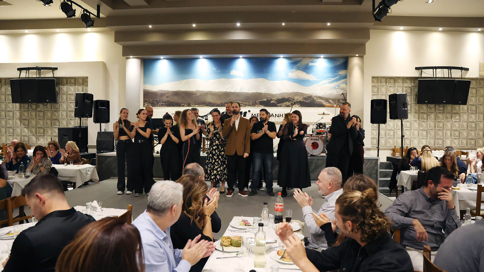 Στη σκηνή εθελοντές όταν άνοιξαν τα φώτα και κόσμος στα τραπέζια χειροκροτούν.