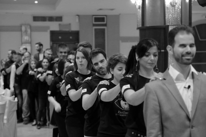 Εθελοντές δείπνου, ο ένας πίσω από τον άλλον, με το δεξί χέρι να αγγίζει τον δεξί ώμο του μπροστινού. Ασπρόμαυρη φωτογραφία.